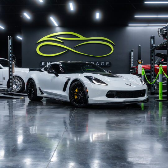 The 2025 Mercedes-Benz G63 AMG in white, parked in a modern garage setting, featuring a sleek exterior design with distinctive grille and aggressive stance. Visible details include black alloy wheels and performance brakes.