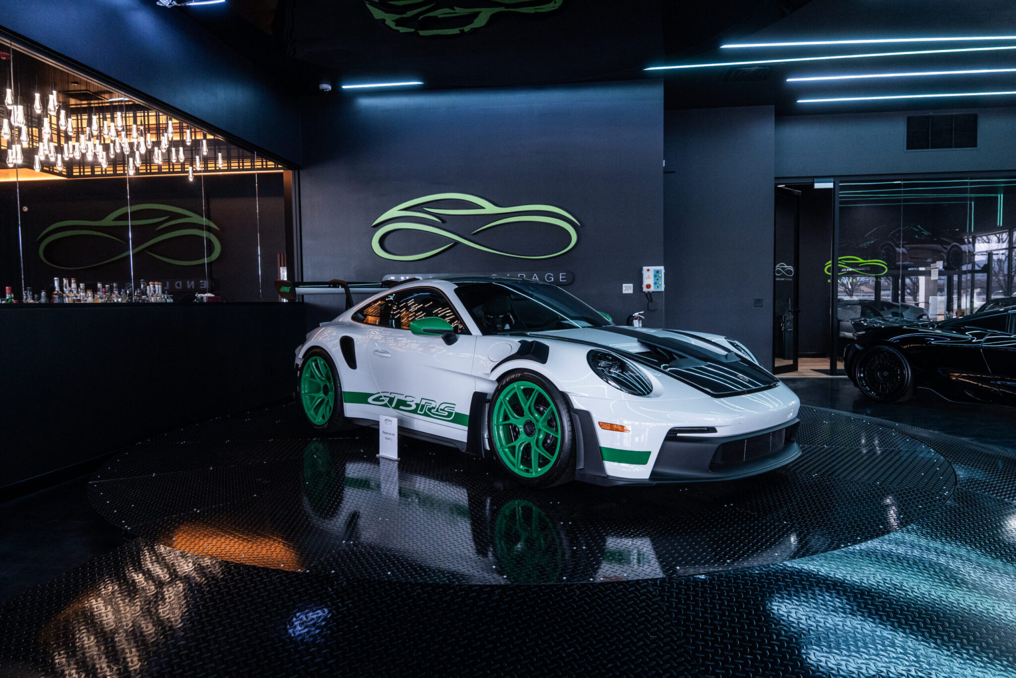 A white sports car with green accents displayed in a modern showroom. The car features a sleek design and is positioned on a glossy black floor with bright lighting and a stylish atmosphere in the background.