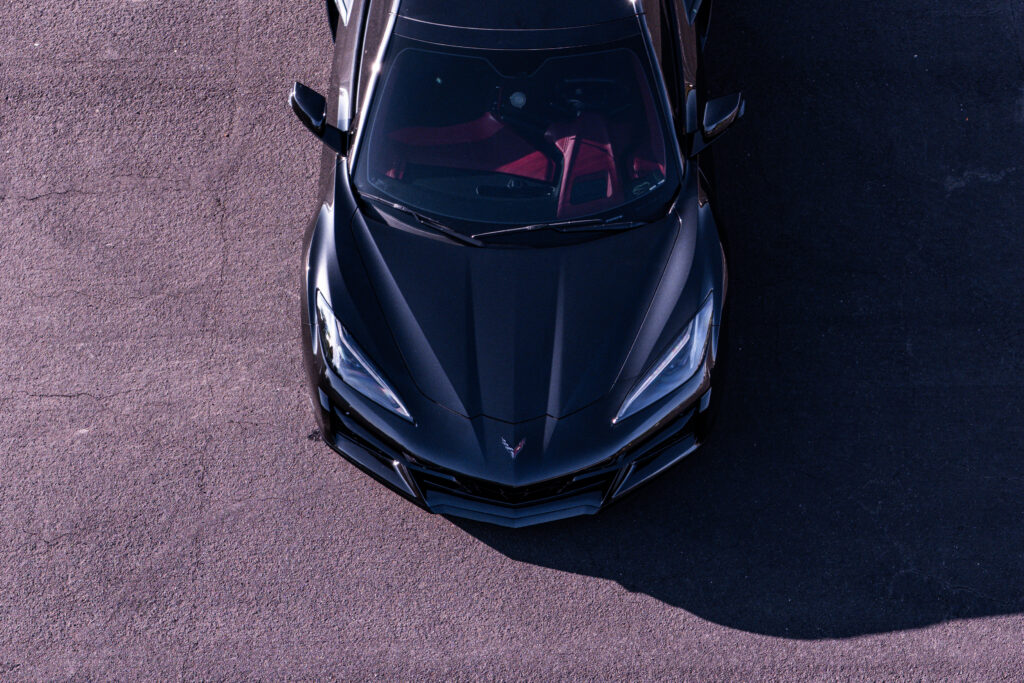 A top-view image of a sleek black sports car with a glossy finish, featuring a distinctive aggressive front design and red interior accents, parked on a neutral-colored surface.