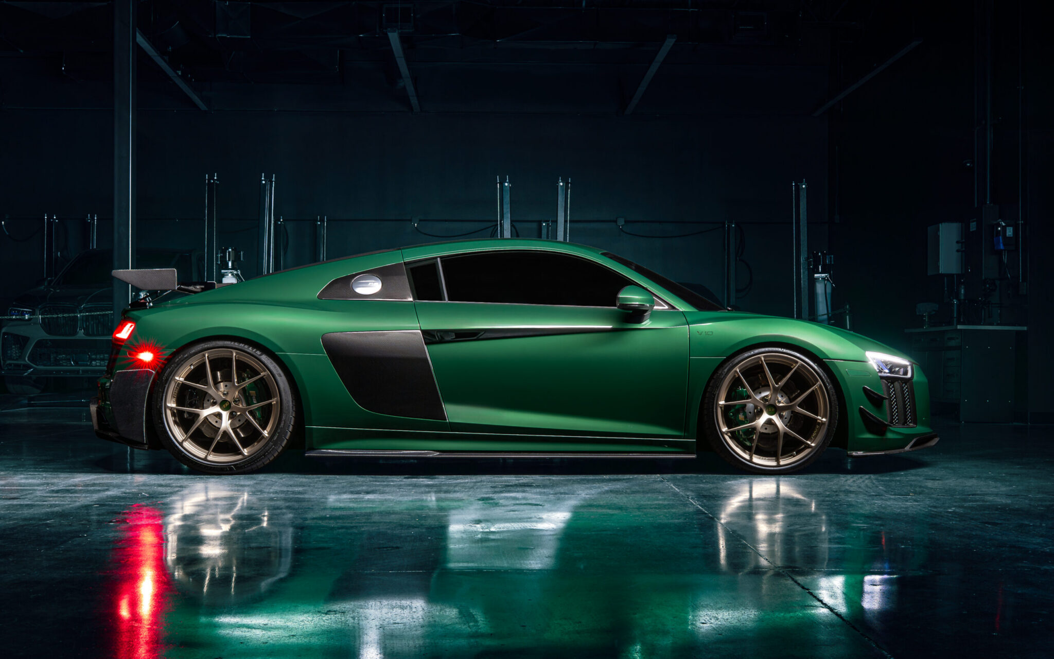 A green sports car with a sleek design and bronze wheels is parked in a dimly lit garage. The car’s profile highlights its aerodynamic shape and glossy finish.